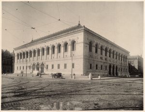 Black and white historic photo of the Boston Public Library, ca. 1925, illustrates the arched openings of the upper floors and the pieced windows of the ground floor of the building.