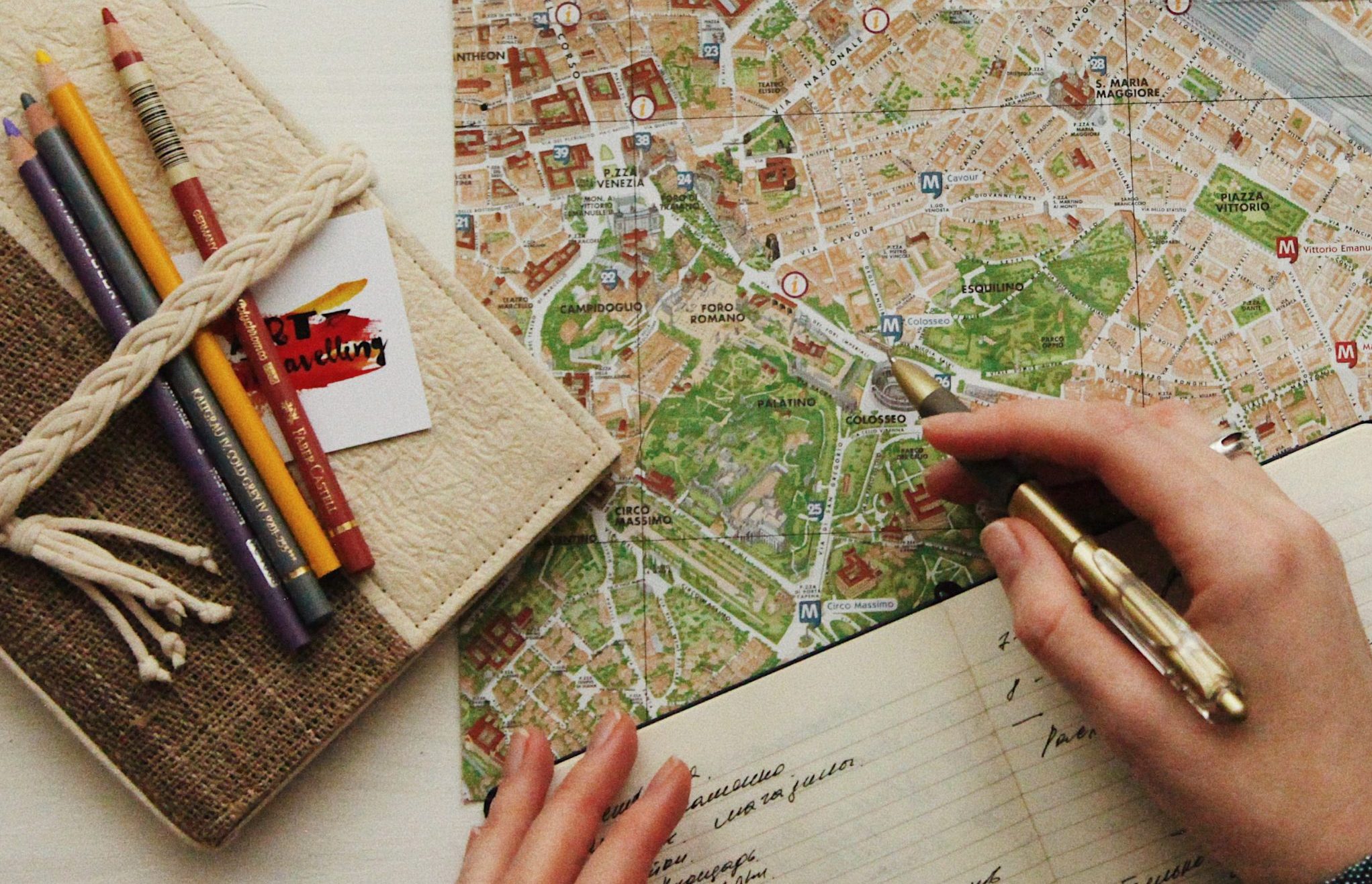 photo of a pair of human hands using a notebook, pen, and a local city street map